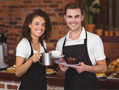 happy male and female cafe staff wearing black apron